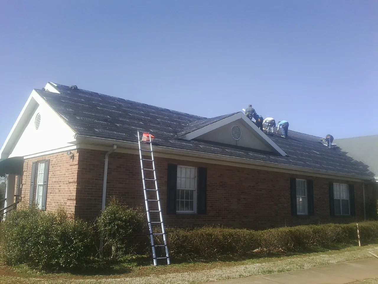Crew tearing shingles off a brick ranch roof with a ladder set — Emergency Roof Repair work by our crew in Hanoverton