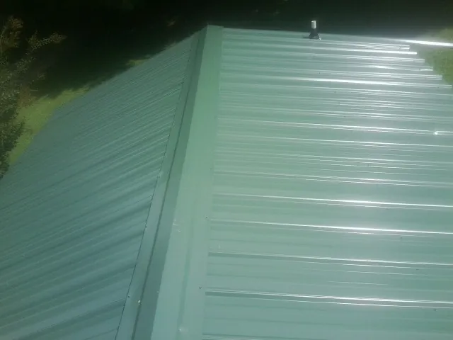 New green metal panels meeting at the ridge of a roof — Flat Roof Repair work by our crew in Hanoverton