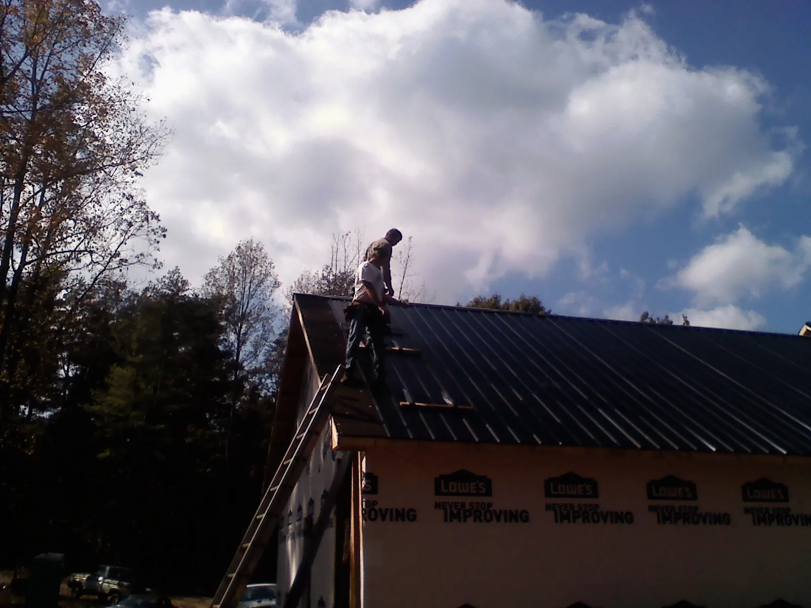 Roofer fastening dark metal panels high against a cloudy sky, from a Roof Inspection job in Hanoverton