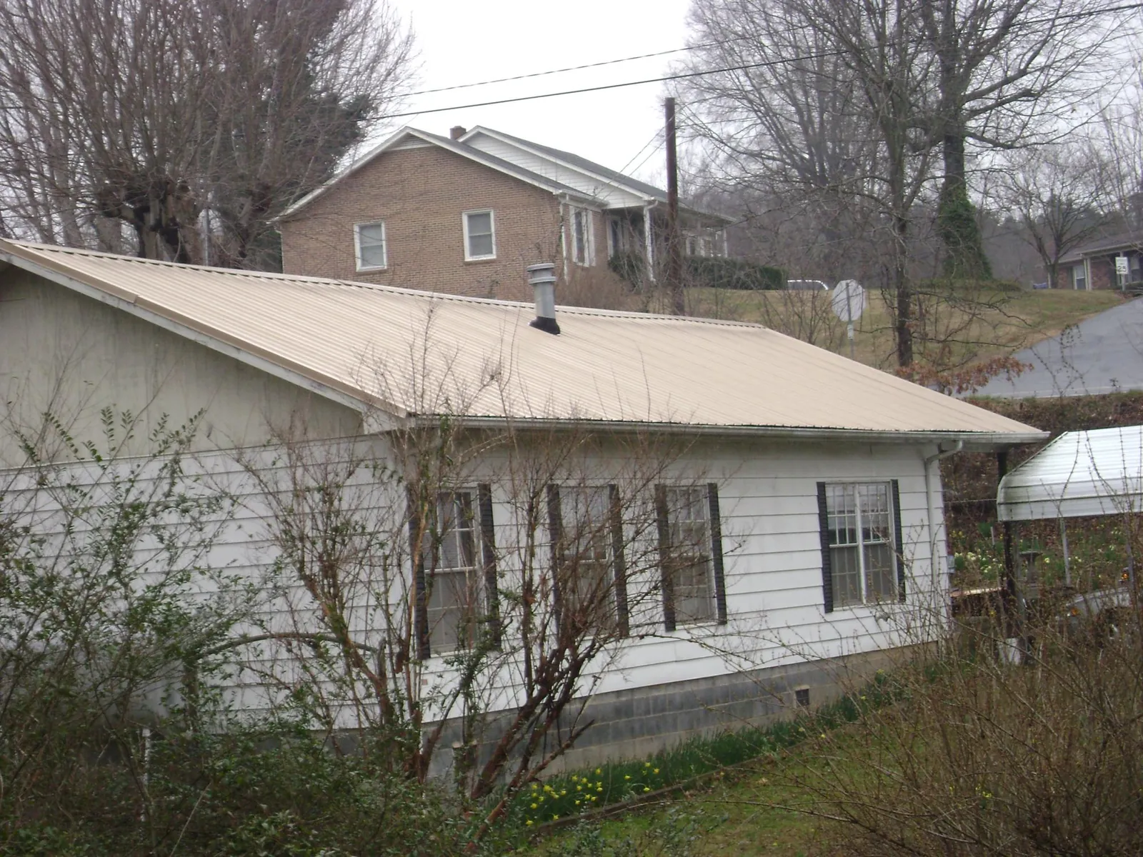Tan metal roof on a white sided house set into a hillside — Commercial Roofing by Roofing Brothers in Hanoverton
