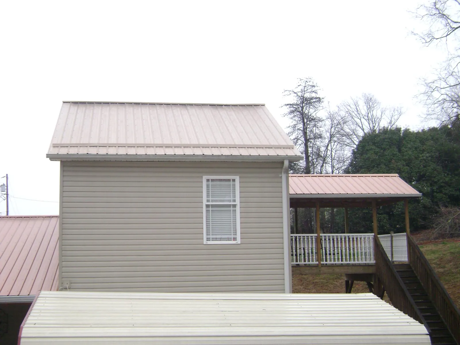 Tan metal roofs on a two story addition and attached porch, from a Roof Replacement job in Hanoverton